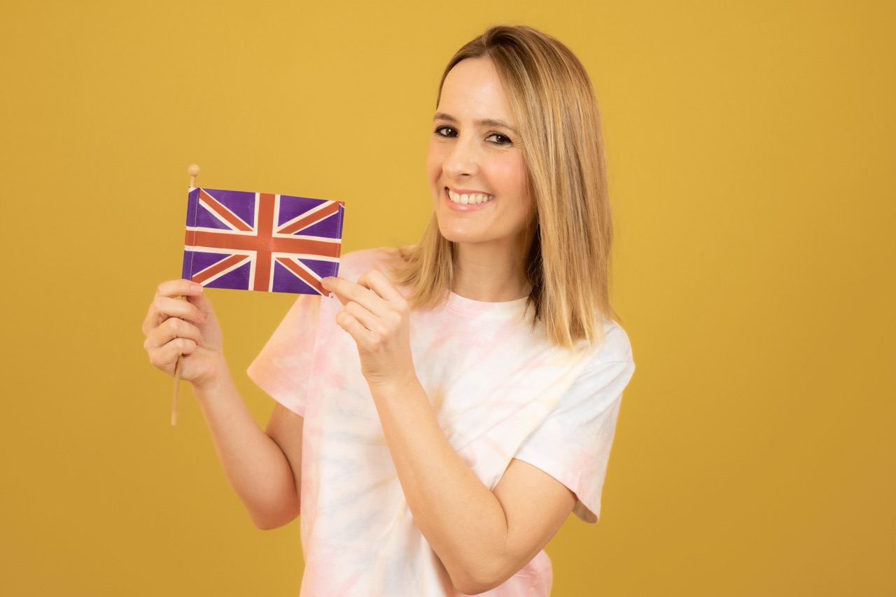 Happy woman with the flag of Great Britain over yellow background.